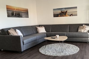 A modern living room with a grey sectional sofa, a round coffee table, and two wall-mounted paintings. - Gertrude's Country House (Juist)