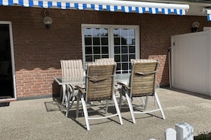 An outdoor patio with a brick wall, a white door, and a covered table and chairs. - Gertrude's Country House (Juist)