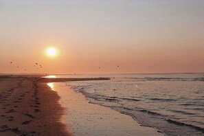 A beach with footprints leading to the water, a clear sky, and the sun low on the horizon. - Holiday apartment with 1 bedroom (Norderney)