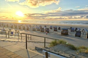A beach with rows of beach chairs and umbrellas, a pedestrian walkway, and a sunset in the background. - Holiday apartment with 1 bedroom (Norderney)