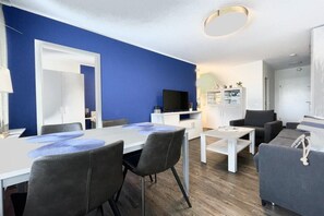 A modern living room with a dining area, a flat-screen TV, and a sofa. - Holiday apartment with 1 bedroom (Norderney)