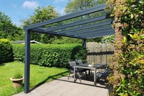 An outdoor patio with a table and chairs, a pergola structure, and a brick wall. - Holiday home with 3 bedrooms (Bruinisse)