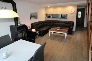 A modern living room with a black leather sofa, a white coffee table, and a dining table with chairs. There is a black TV stand with a lamp, a small plant, and a picture on the wall. - Holiday home with 3 bedrooms (Bruinisse)