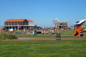 A public park with a playground, a building with a red roof, and a body of water in the background. - Holiday home with 3 bedrooms (Bruinisse)