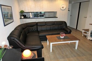 A modern living room with a sectional sofa, a wooden coffee table, and a kitchen area in the background. - Holiday home with 3 bedrooms (Bruinisse)