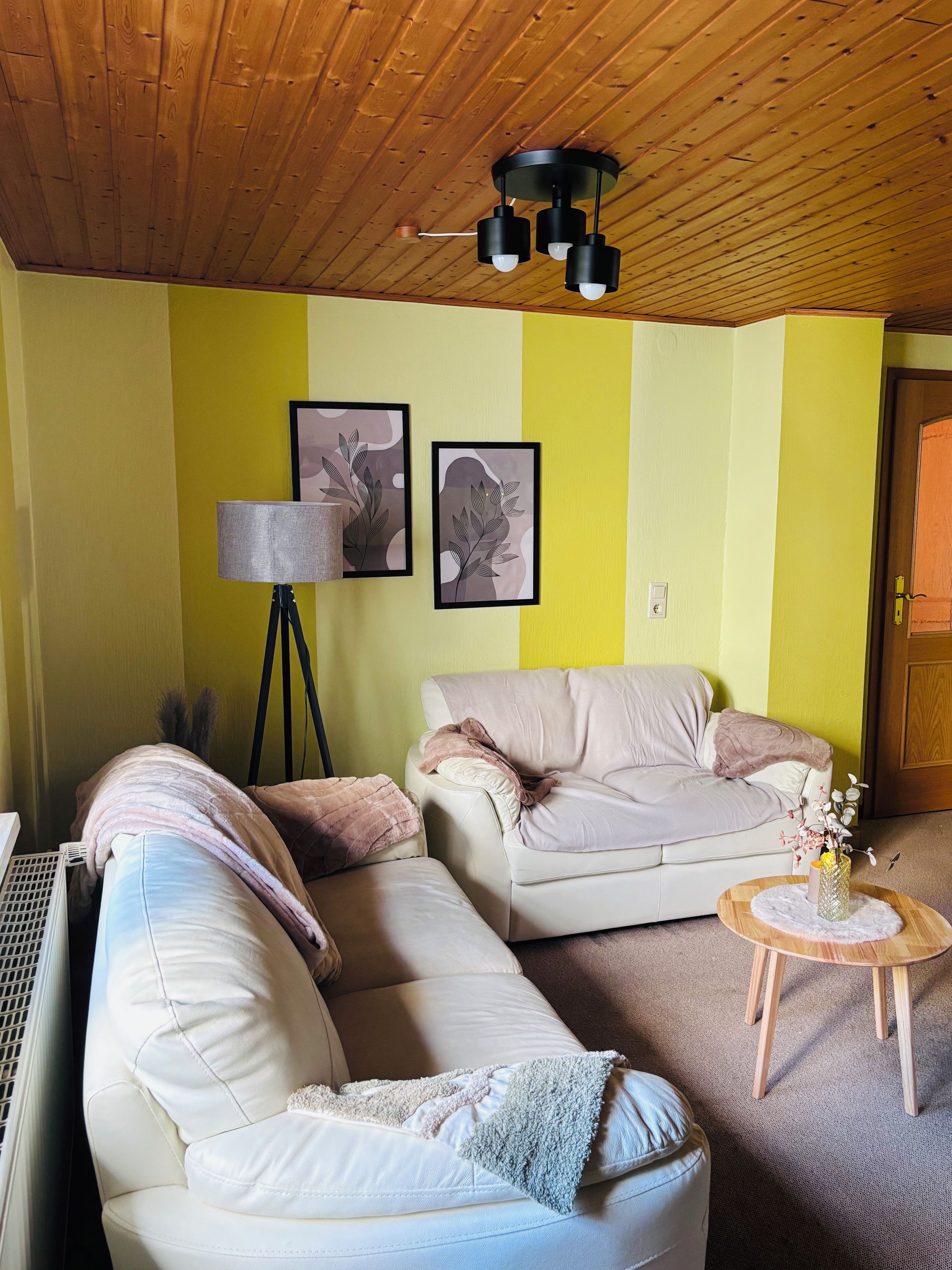 Ein Wohnzimmer mit zwei Sofas, einer Lampe und gerahmten Kunstwerken an der Wand.