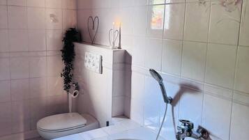 Ein Badezimmer mit Badewanne, Toilette, Dusche und einem fest installierten Toilettenpapierhalter.