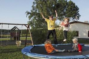 A trampoline in an outdoor setting with a swing set and a building in the background. - Country holiday Müritz (Jabel)