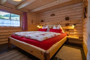 A wooden cabin bedroom with a bed, a window with curtains, and wall-mounted lights. - Conny's Nature Mountain Hut (Grosskirchheim)