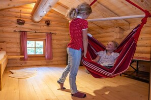 A wooden cabin interior with a hammock, a window with checkered curtains, and a bed. - Conny's Nature Mountain Hut (Grosskirchheim)