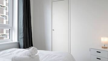 A bedroom with a bed, a window with curtains, a wardrobe, and a bedside table with a lamp.
