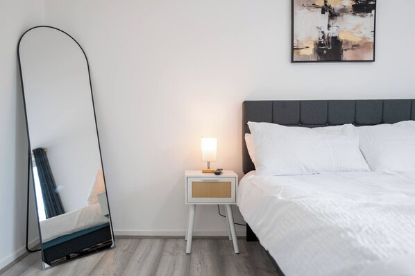 A bedroom with a bed, a nightstand with a lamp, a mirror, and a painting on the wall. - Modern 3BD Flat Hoxton & Shoreditch N1 (London)