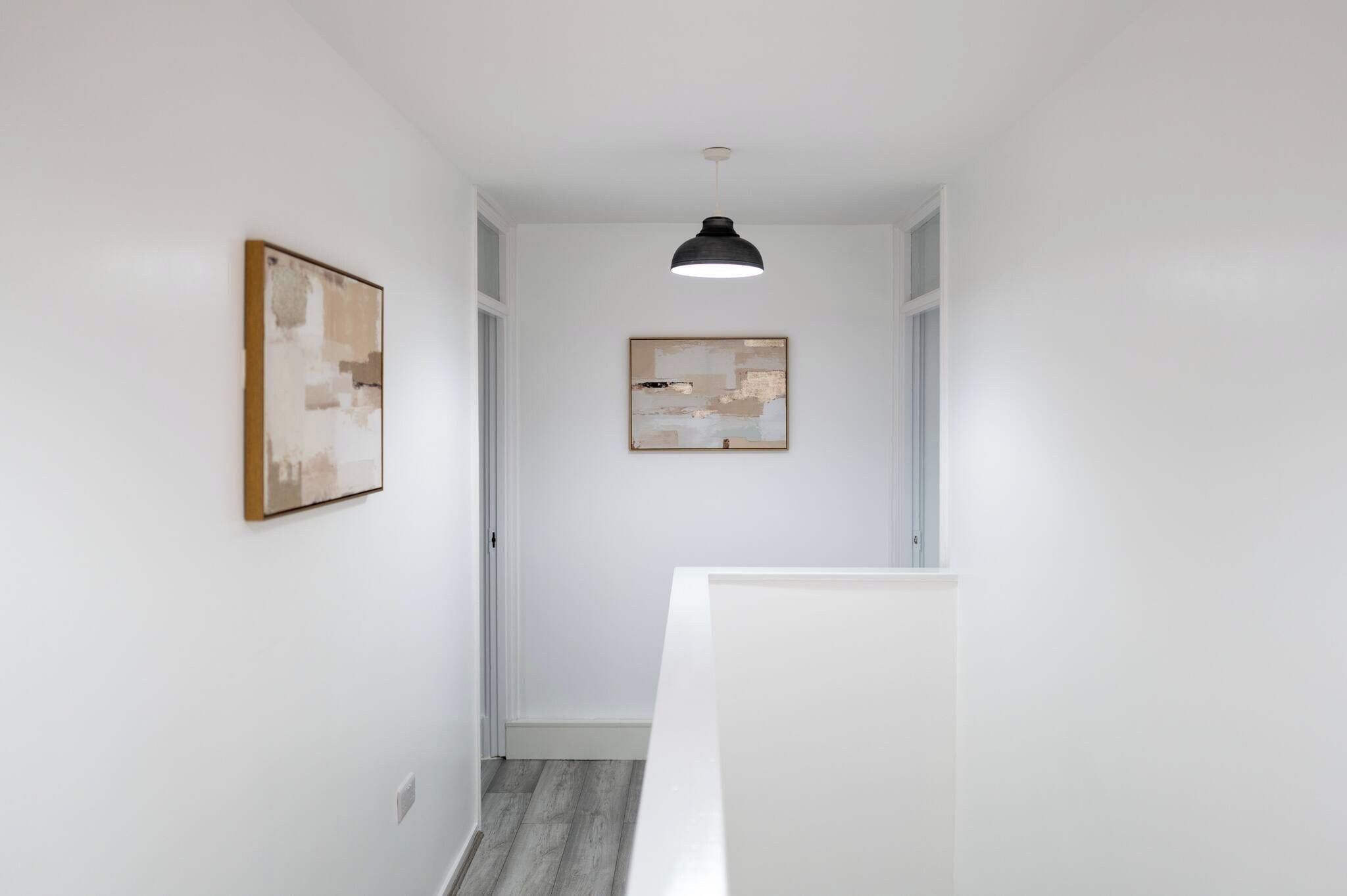 A hallway with white walls, a ceiling light, and two framed artworks.