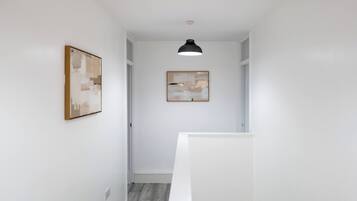A hallway with white walls, a ceiling light, and two framed artworks.