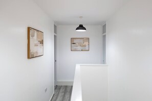 Ein Flur mit weißen Wänden, einer Deckenleuchte und zwei gerahmten Kunstwerken.