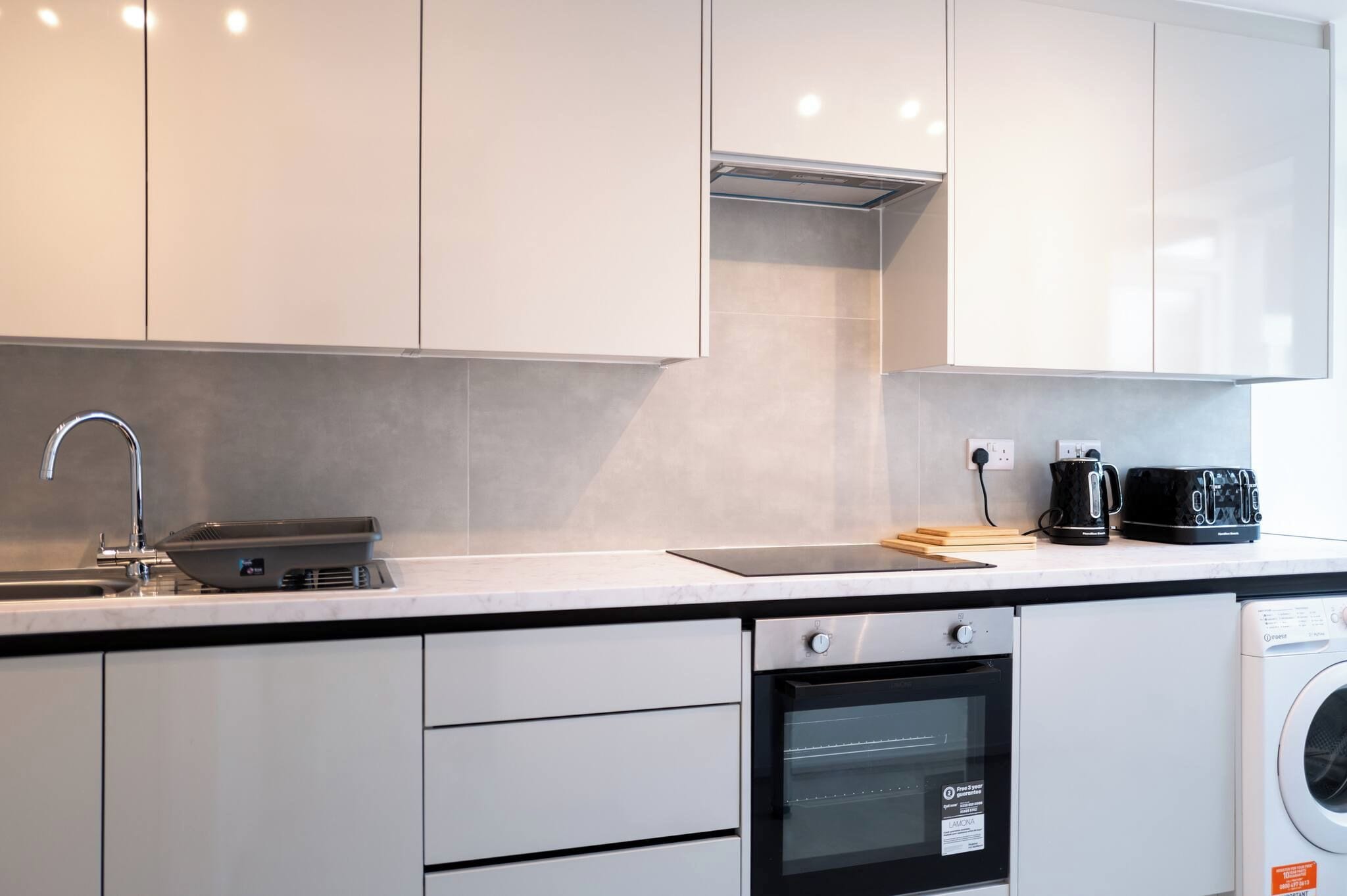 A modern kitchen with white cabinets, a stainless steel sink, a coffee maker, and a built-in oven.