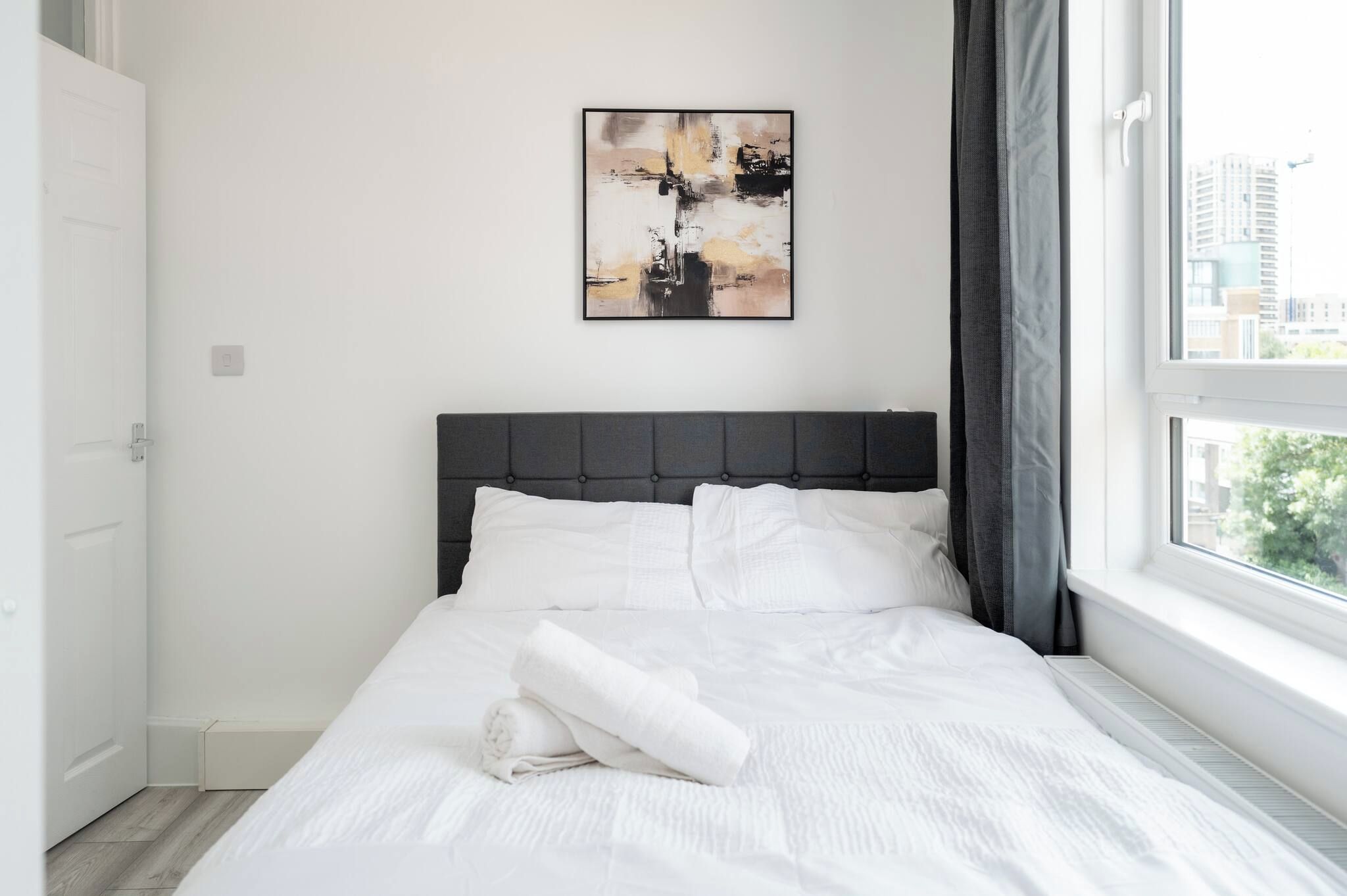 A modern bedroom with a bed, a painting, and a window with curtains.