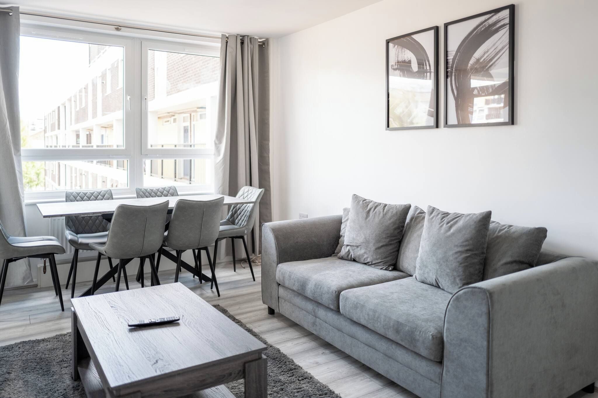 A modern living room with a grey sofa, a wooden coffee table, and a dining area with chairs and a table.