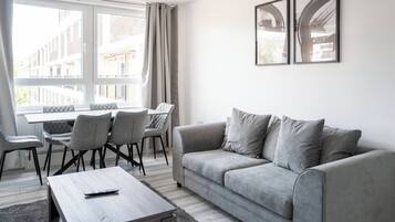 A modern living room with a grey sofa, a wooden coffee table, and a dining area with chairs and a table.