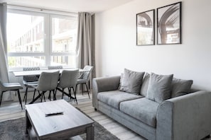 A modern living room with a grey sofa, a wooden coffee table, and a dining area with chairs and a table. - Modern 3BD Flat Hoxton & Shoreditch N1 (London)