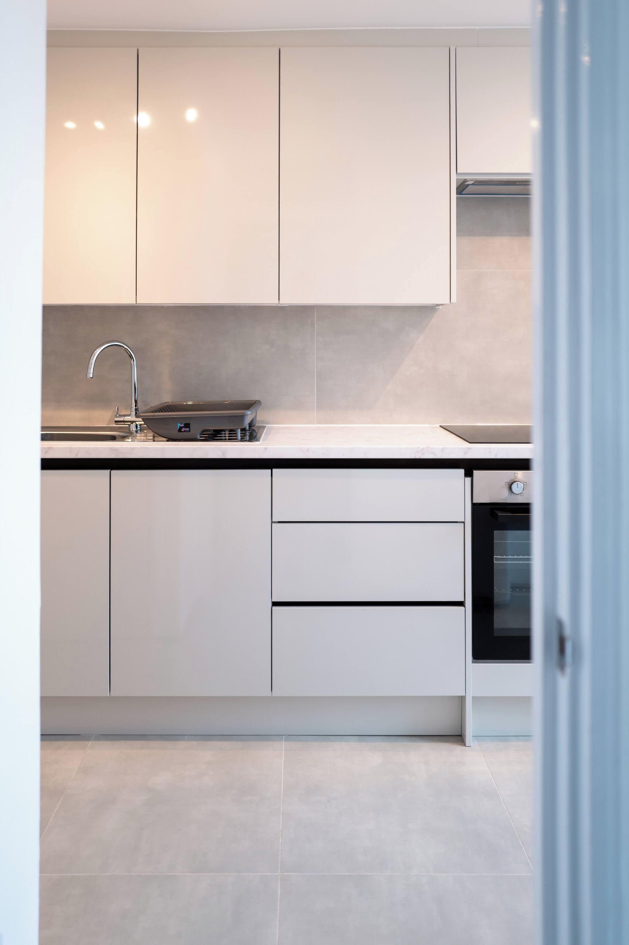 A modern kitchen with white cabinetry, a built-in oven, and a stainless steel sink.