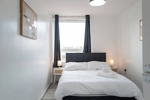 A hotel room with a bed, bedside tables, a window with curtains, and a view of the city. - Modern 3BD Flat Hoxton & Shoreditch N1 (London)