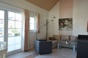 A living room with a sofa, a glass coffee table, a modern floor lamp, and a painting on the wall. - Holiday apartment with 2 bedrooms (Wendisch Rietz)