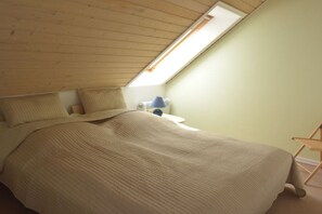 Et soveværelse med skråvæg, seng, natbord, lampe og stol.