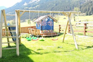 A wooden swing set with a blue birdhouse and a wooden deck. - Holiday apartment in Maishofen with sauna (Maishofen)