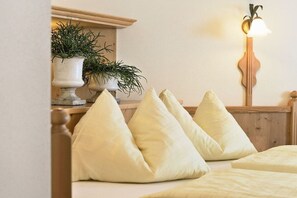 A bed with a wooden headboard, multiple pillows, a bedside table with a potted plant, and a wall-mounted lamp. - Apartment in Dorfgastein with swimming pool (Dorfgastein)