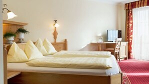 Een hotelkamer met een tweepersoonsbed, nachtkastjes, een bureau met stoel, een televisie en een rood tapijt.