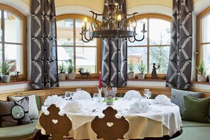 A dining area with a round table set for a meal, large windows, and a chandelier. - Apartment in Dorfgastein with swimming pool (Dorfgastein)