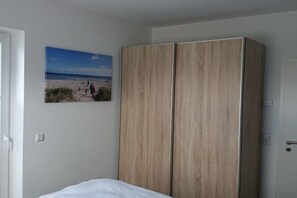 Ein Schlafzimmer mit einem Bett, einem Holzschrank und einem Bild mit Strandmotiv an der Wand.