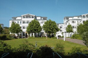 A large, white, multi-story building with a symmetrical facade, surrounded by a well-maintained lawn and trees. - Holiday apartment 49 Villa Louisa (Sellin)
