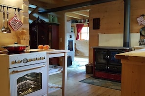 A wooden interior with a white stove, a black oven, and a table with a red pot. - Holiday home in Gosau with swimming pool (Gosau)