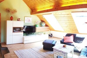 A cozy living room with a television, sofa, and a small table with fruit. - Holiday apartment with 1 bedroom (Seeboden)