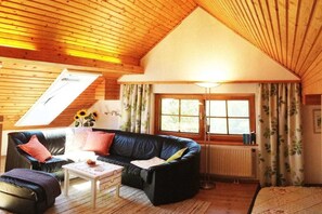 A cozy room with a sloped ceiling, a black leather sofa, a white coffee table, and a window with curtains. - Holiday apartment with 1 bedroom (Seeboden)