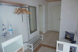 Ein Zimmer mit einem weißen Kleiderschrank, einem kleinen Tisch mit einer Flasche, einer Bank und einer Tür im Hintergrund.