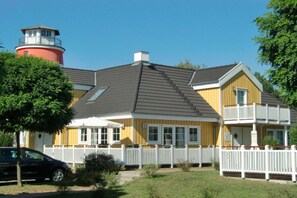 A yellow building with a white fence, a red tower, and a black car parked in front. - House Scharmützelsee (Wendisch Rietz)