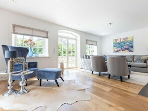 A spacious living room with a large window, a modern sofa set, and a decorative rug. - Holiday Home Pidder Hus Kampen / Sylt (Kampen)