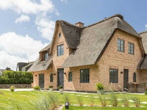 A traditional brick house with a steeply pitched thatched roof, multiple windows, and a well-maintained lawn. - Holiday Home Pidder Hus Kampen / Sylt (Kampen)