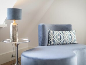 A room with a round, blue upholstered chair, a patterned pillow, and a modern floor lamp with a cylindrical shade. - Holiday Home Pidder Hus Kampen / Sylt (Kampen)