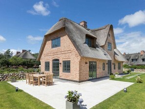 A large brick house with a thatched roof, a patio with outdoor furniture, and a well-maintained garden. - Holiday Home Pidder Hus Kampen / Sylt (Kampen)