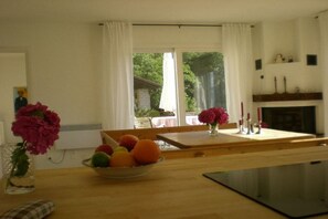 Ein Essbereich mit einem Holztisch, einer Obstschale und einer Vase mit Blumen.