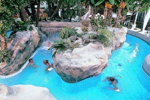 Ein Schwimmbecken mit Wasserfall, umgeben von tropischer Vegetation und Felsen.