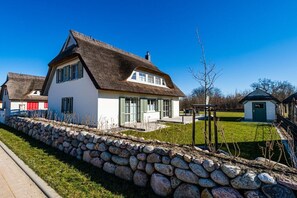 A house with a thatched roof, a stone wall, and a small garden. - Holiday home with 1 bedroom (18445 Kramerhof, Deutschland)