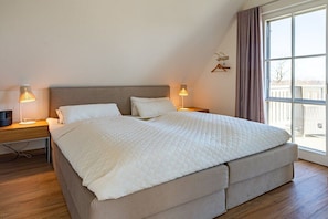 Ein Schlafzimmer mit einem großen Bett, zwei Nachttischen, einem Fernseher und einem Fenster mit Vorhängen.