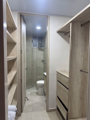 Een smalle badkamer met een douche, toilet en houten planken.