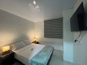 Een hotelkamer met een bed, bedlampen, een aan de muur bevestigde televisie en een raam met jaloezieën.
