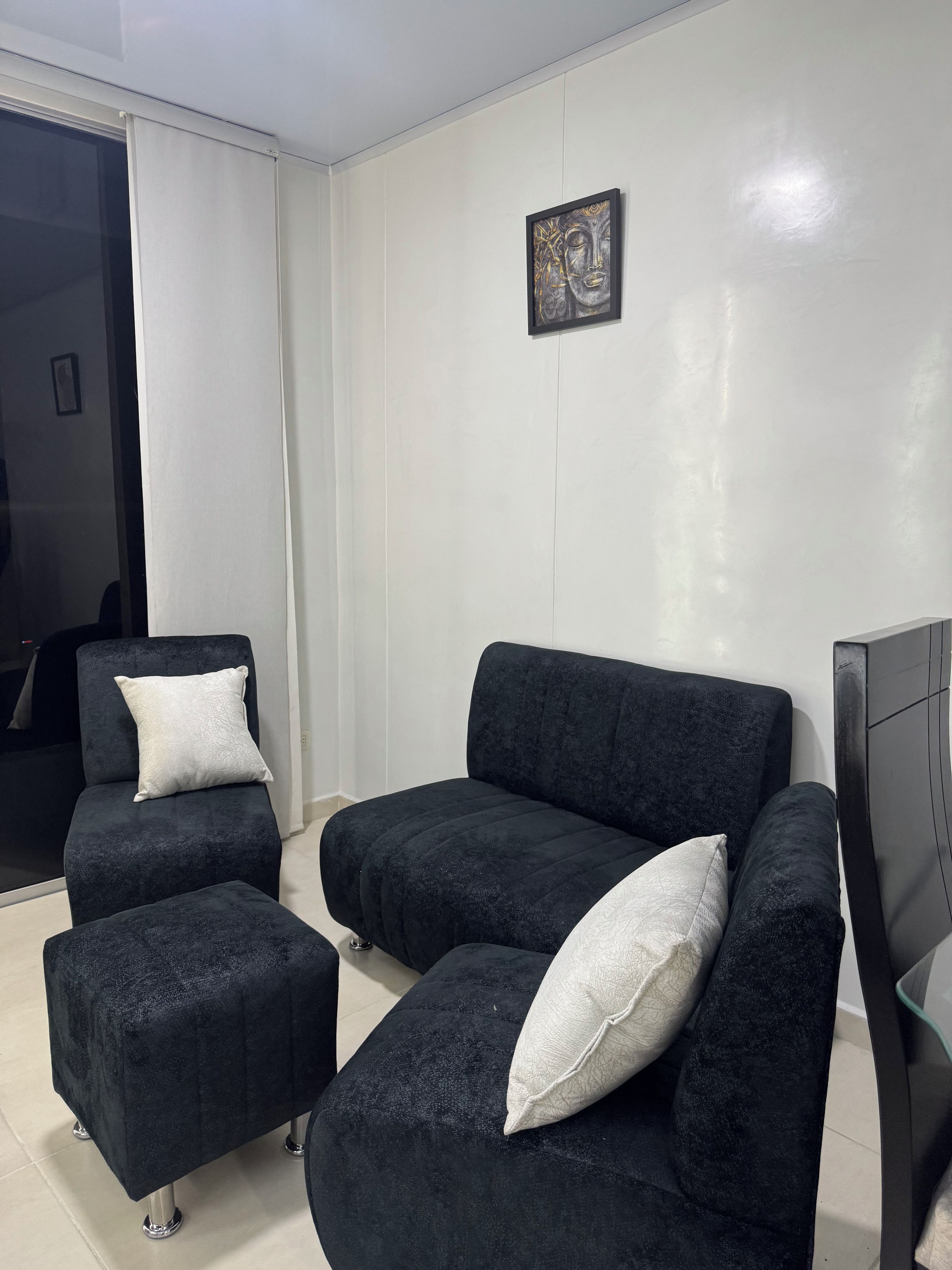 A modern living room with a dark-colored sofa set, a small ottoman, and a framed artwork on the wall.